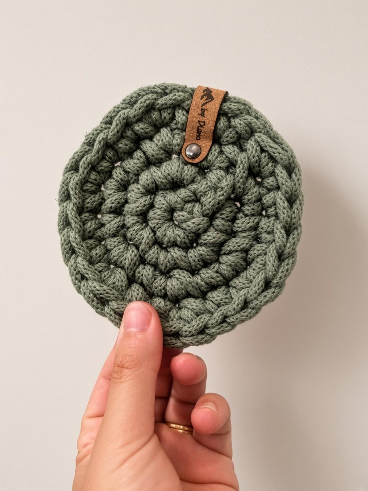 Sage green crochet coaster held between fingers